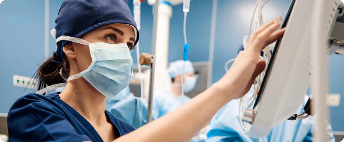 Nhân viên y tế đeo khẩu trang và mũ phẫu thuật vận hành thiết bị theo dõi trong phòng bệnh.