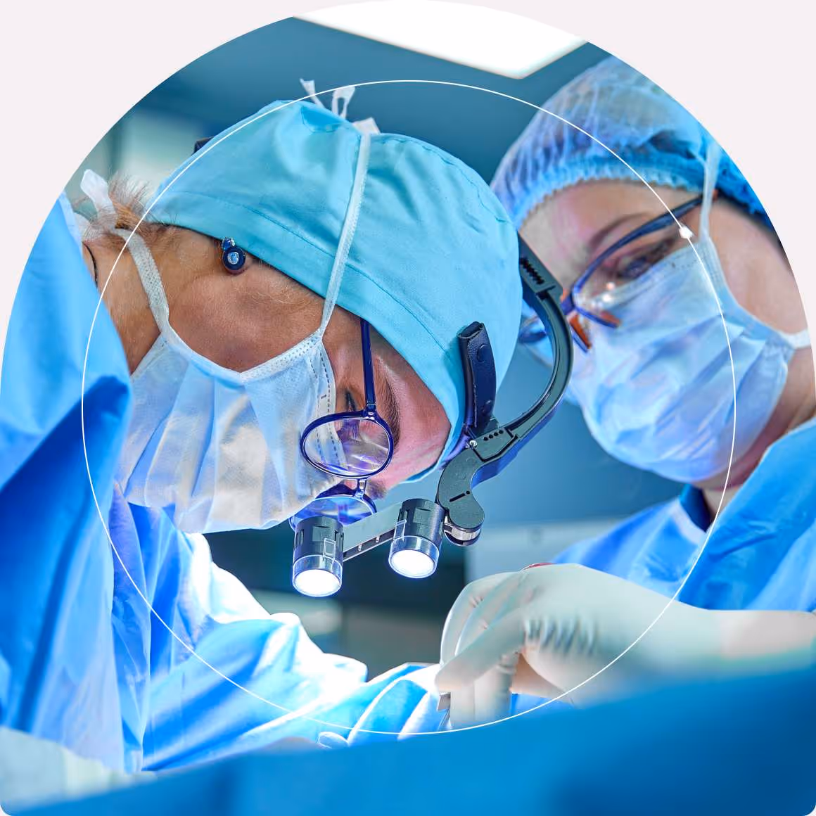 Hai bác sĩ mặc đồ mổ màu xanh đang thực hiện thủ thuật, một người đeo đèn đội đầu.